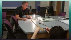 photo showing one person looking through a diffraction grating at a light bulb