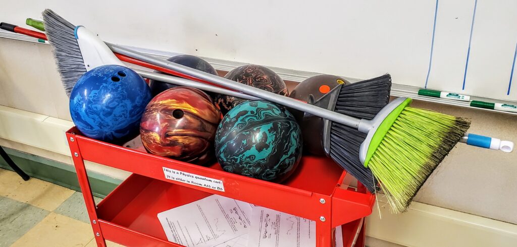 photo showing bowling balls on a red cart with a couple of brooms laid sideways on top